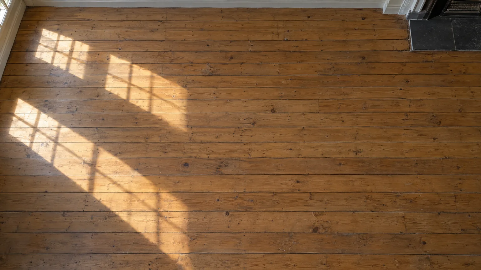 An empty timber floor in an old stone house, seen from above, with bands of morning sun across the boards