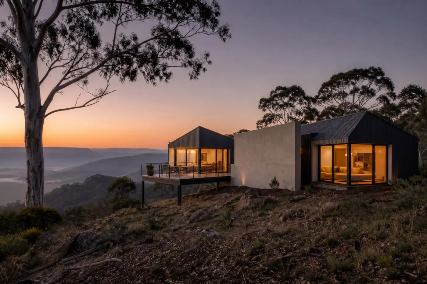 The Stirling ridge house at dusk, two dark pavilions and a warm blade wall with a deck cantilevered over a misty valley