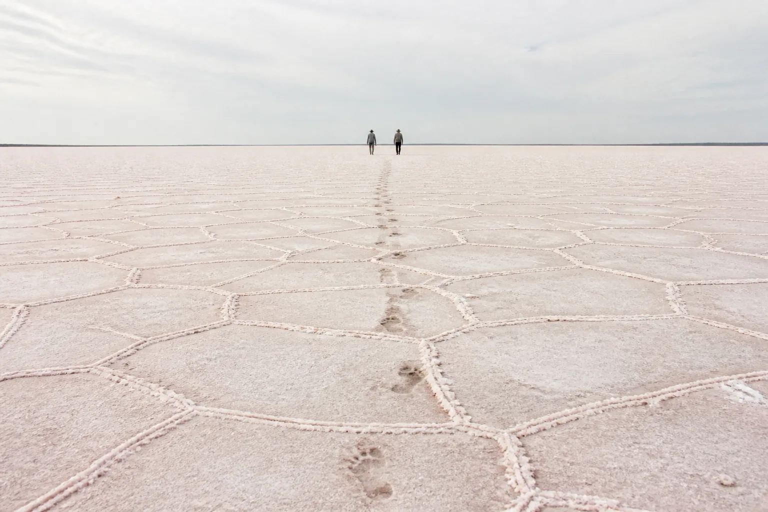 White salt crust to a flat horizon, a line of footprints leading to two small walkers