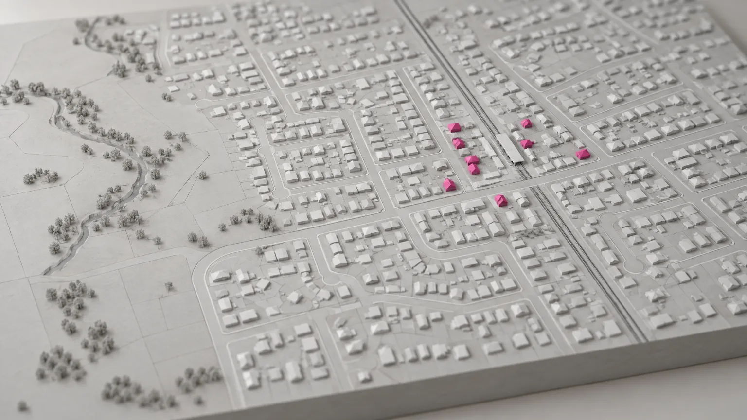 A white clay model of a suburb seen from above, most homes pressed flat and a few near the station standing in pink