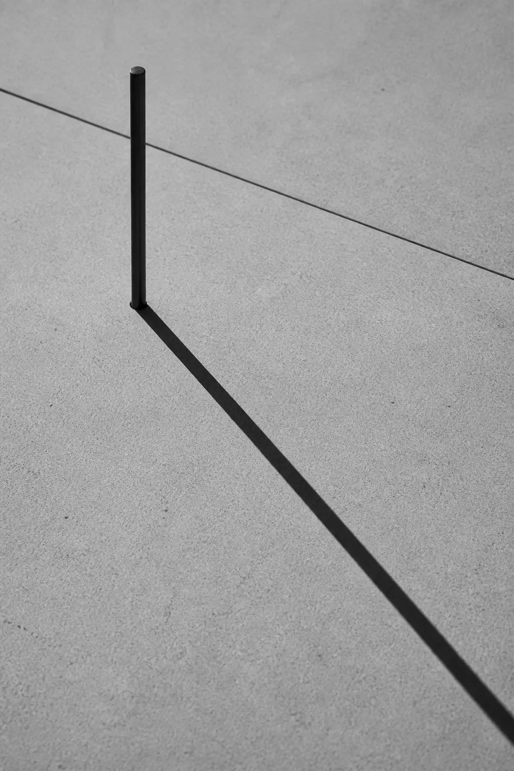 A slender steel pin standing in pale stone, its long thin shadow running across the slab.