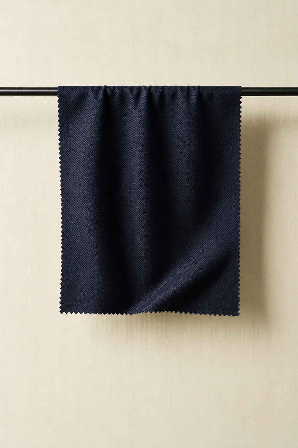 A square of midnight navy twill hangs from a black rod, folding softly against a calico backdrop.
