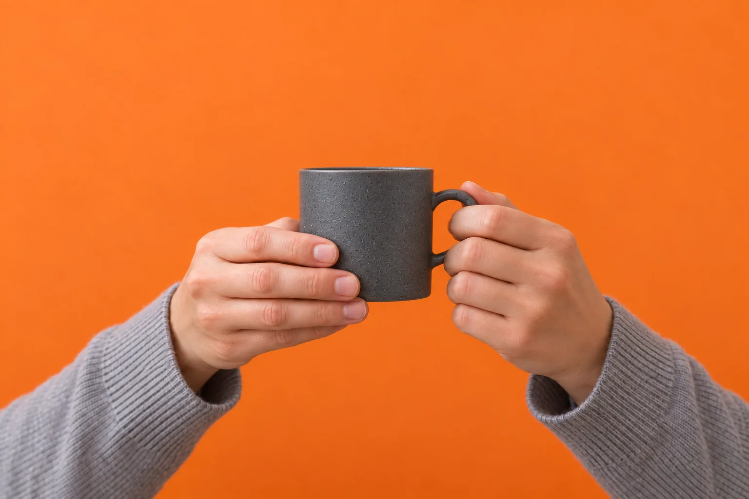 Two hands in grey sleeves holding a graphite cup against orange.
