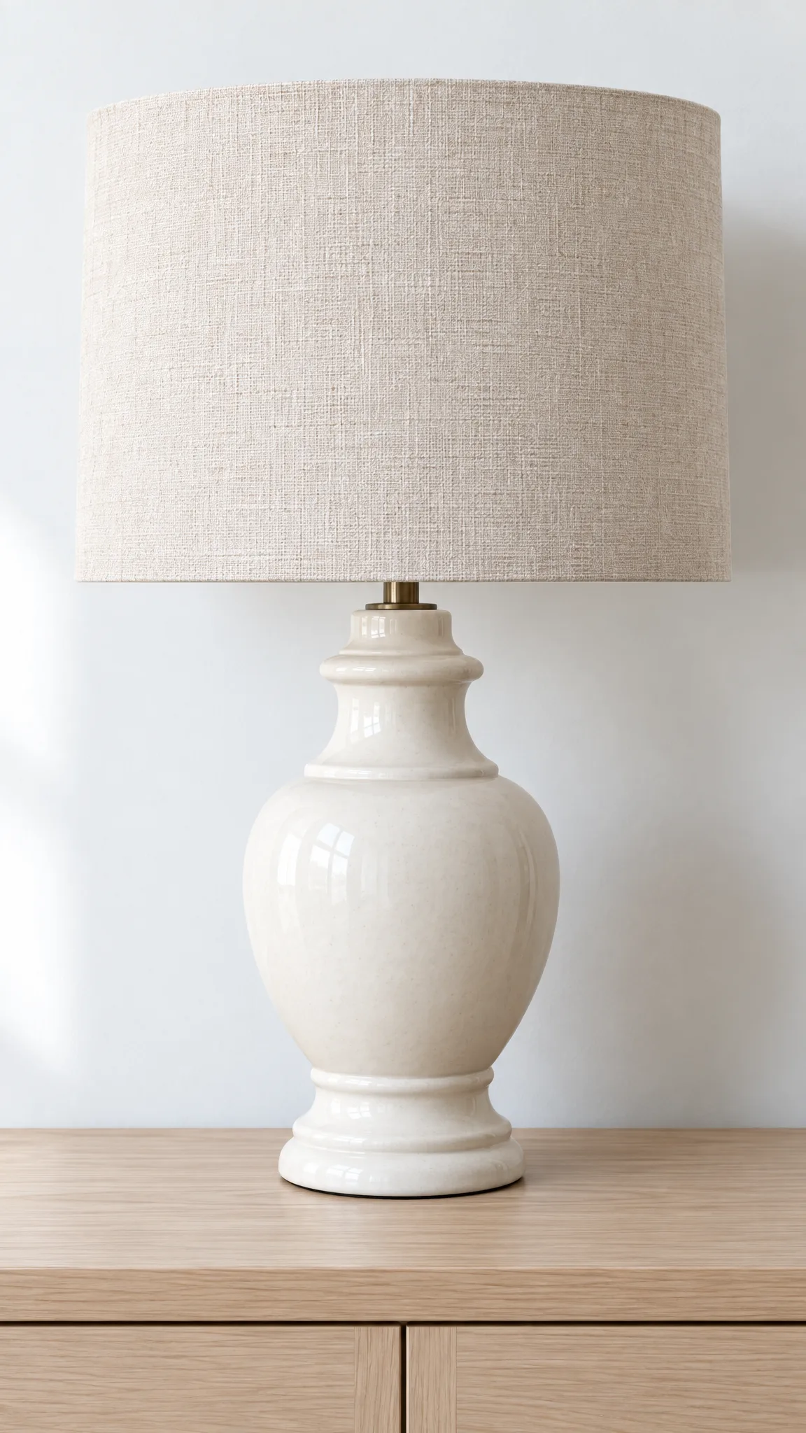 An unlit white ceramic lamp with a linen shade on a pale ash sideboard.