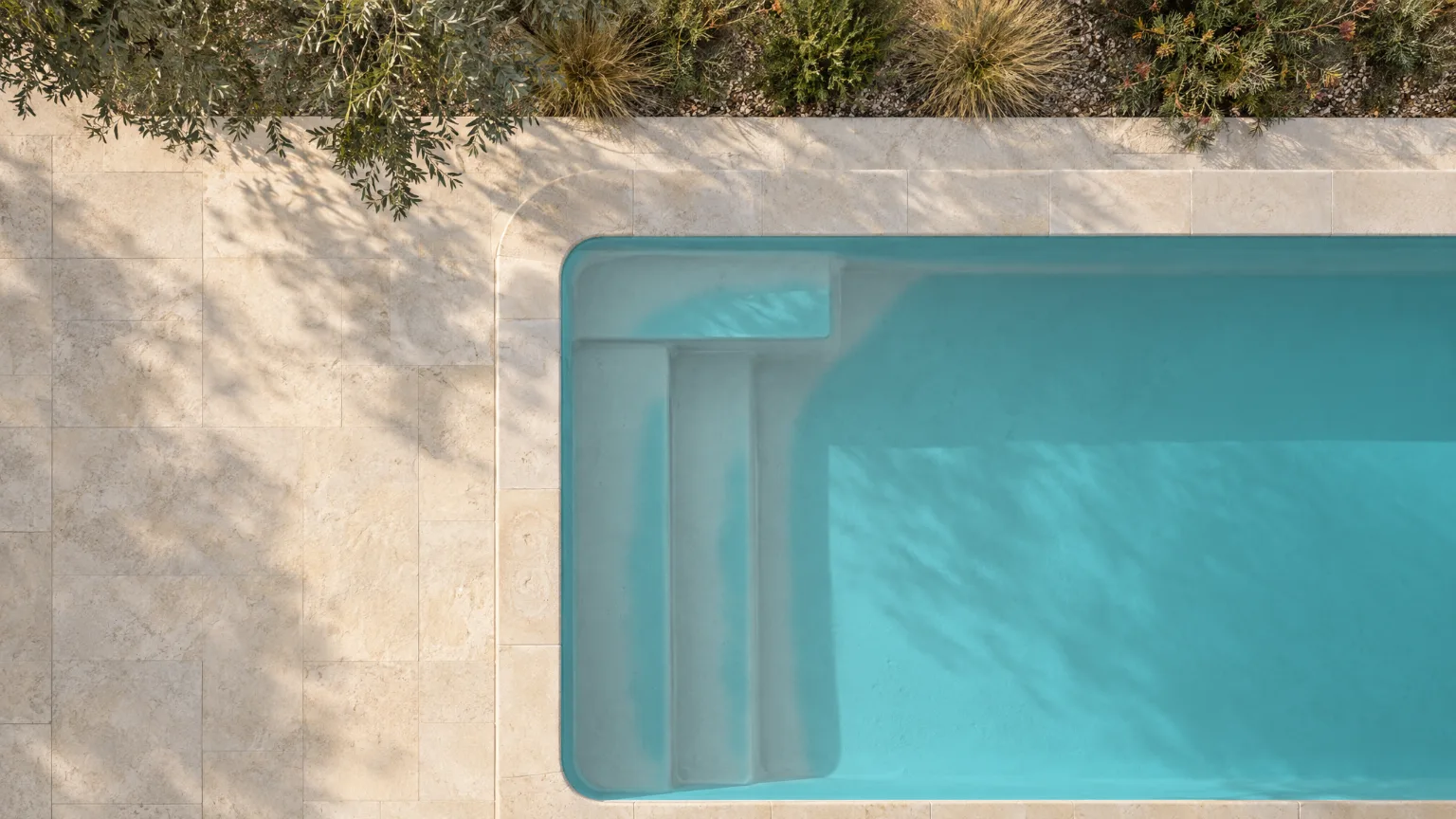 Straight down on a pool in a pale limestone terrace, its water turquoise over white render, a broad step at the near end.