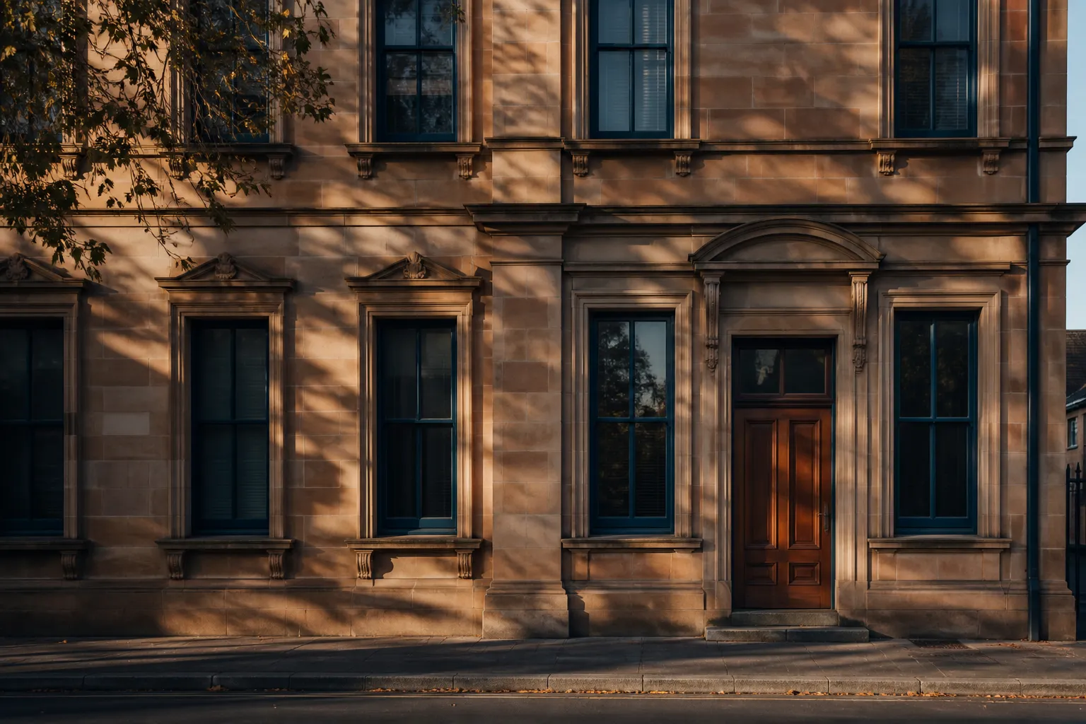 A sandstone office facade with ink-blue window frames and a timber door, lit by low afternoon sun