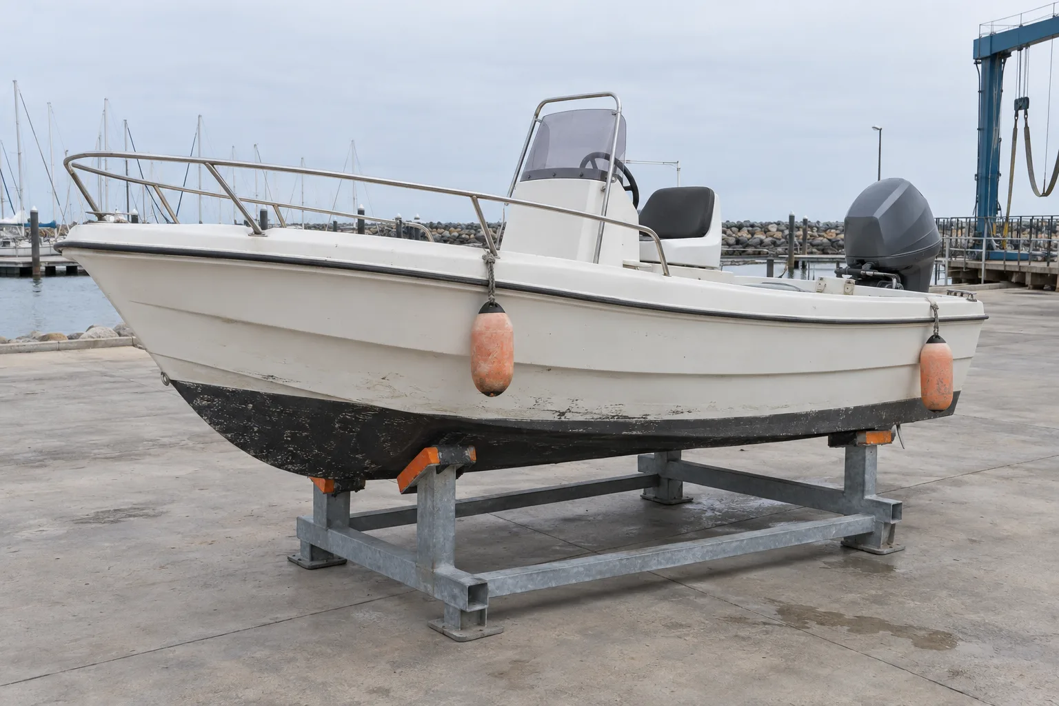 The Bay 03 runabout on a steel cradle on grey concrete, orange fenders hanging from its rail.