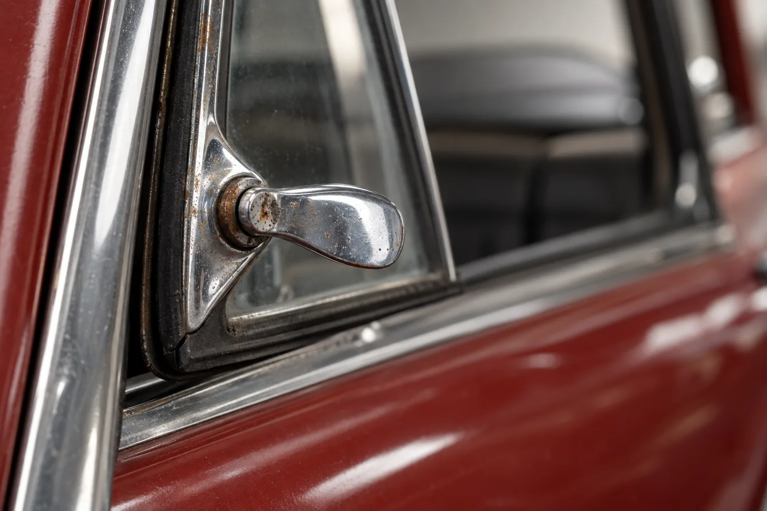The chrome catch of the shooting brake's quarterlight, pitted at the pivot, the red door beyond