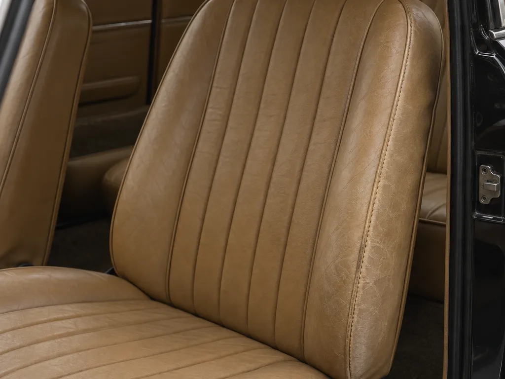 The fastback's tan driver's seat through the open black door, one bolster seam sewn again in a lighter thread