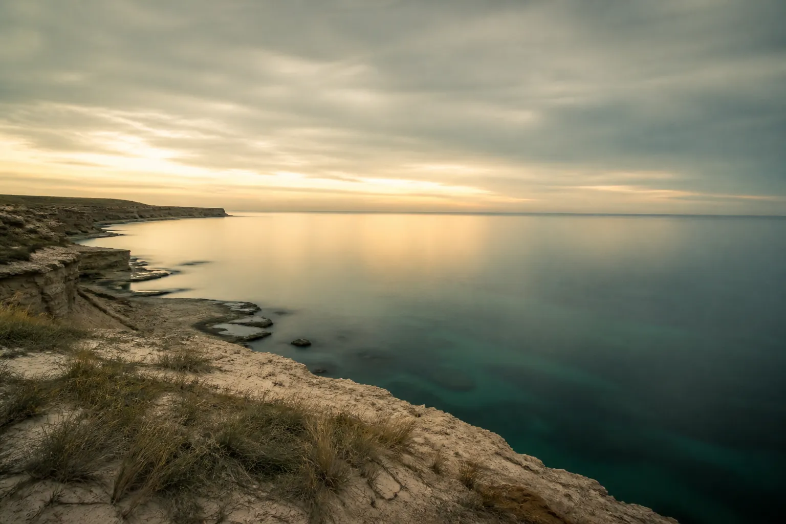 A low limestone coastline and a still gulf sea under a pale dawn sky