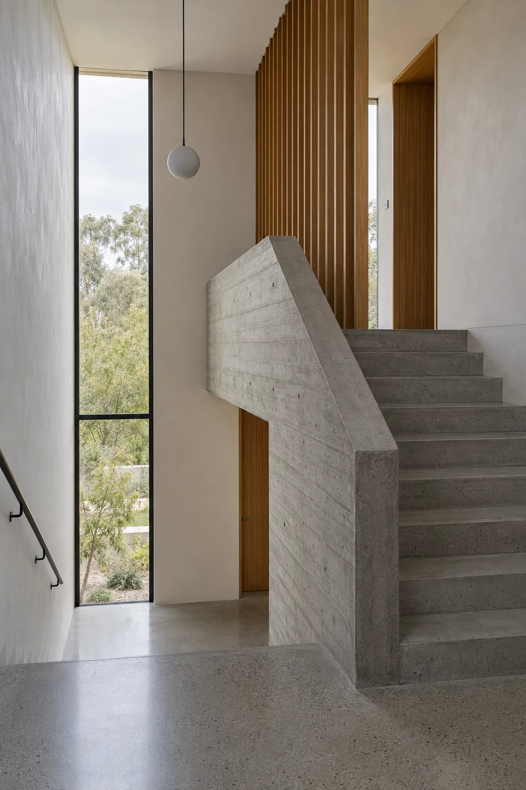 A folded concrete stair beside a timber batten screen, lit by a tall slot window.
