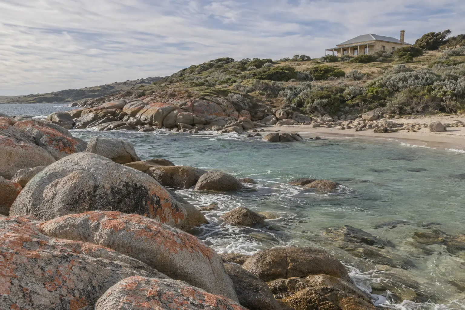 A pale limestone house on a grassy rise above a cove of lichen-covered granite boulders