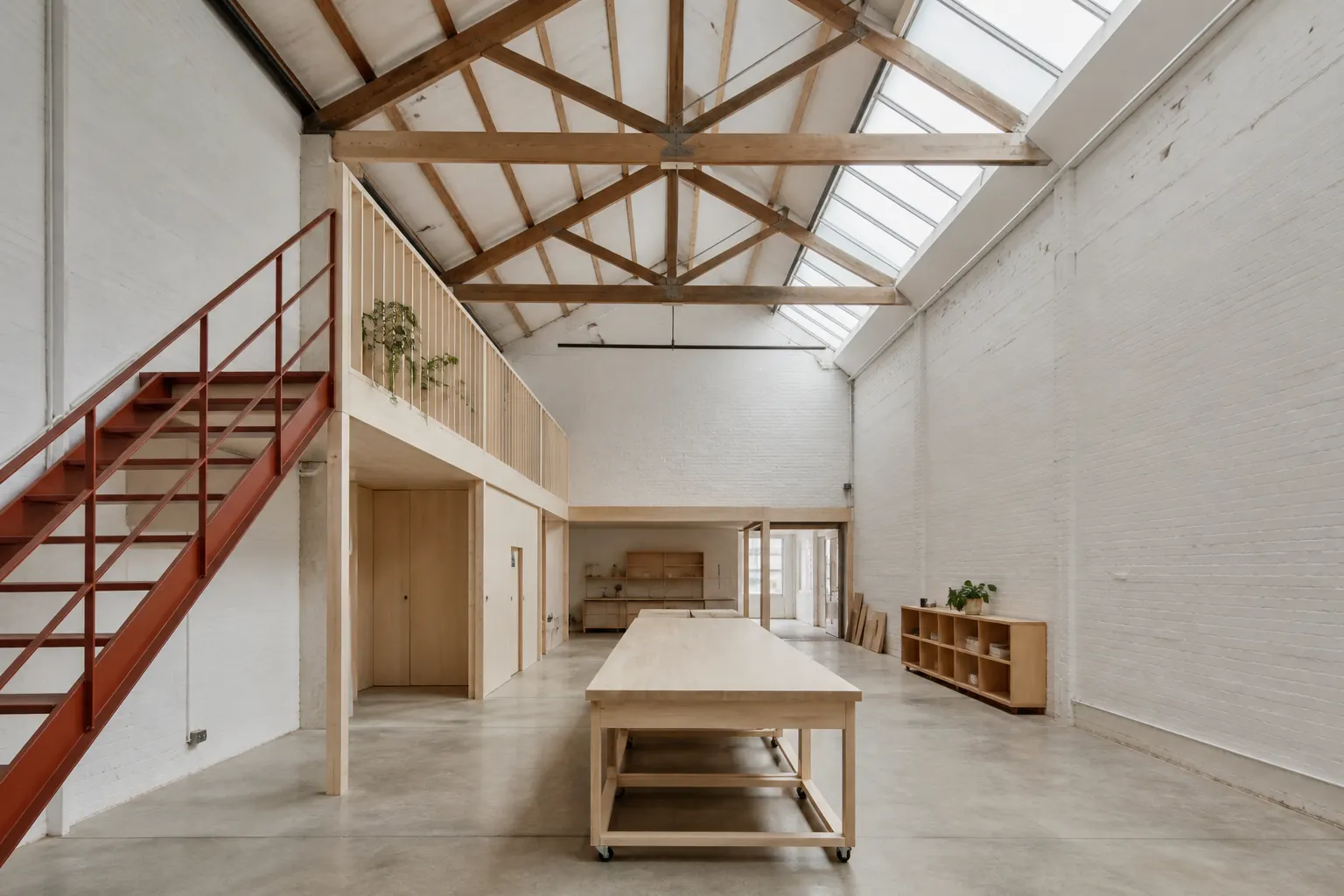 Hindmarsh warehouse studio: a tall whitewashed brick volume with timber trusses, a sawtooth skylight, a new timber mezzanine and a clay-red steel stair
