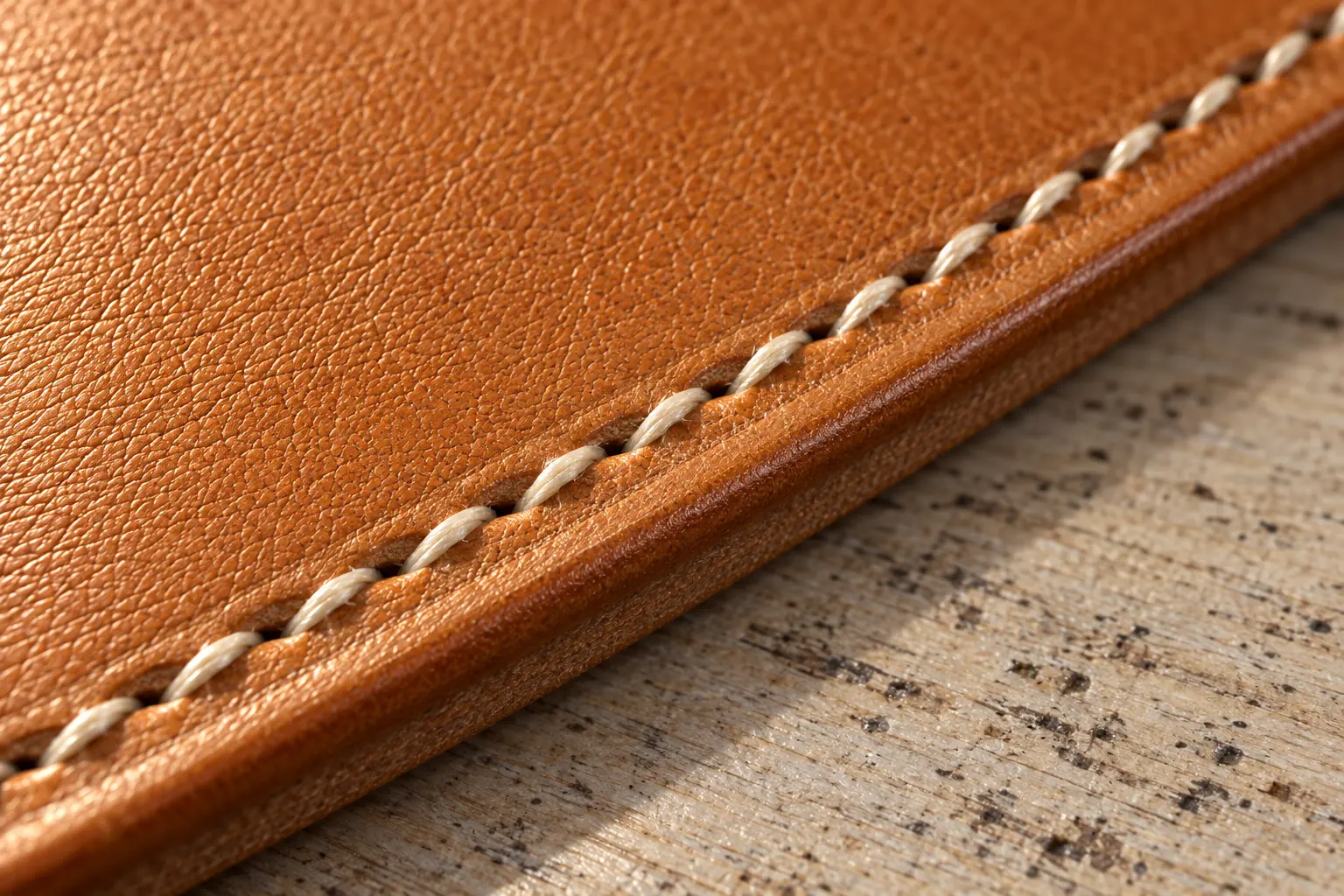 Slanted cream saddle stitches running along a burnished tan leather edge.
