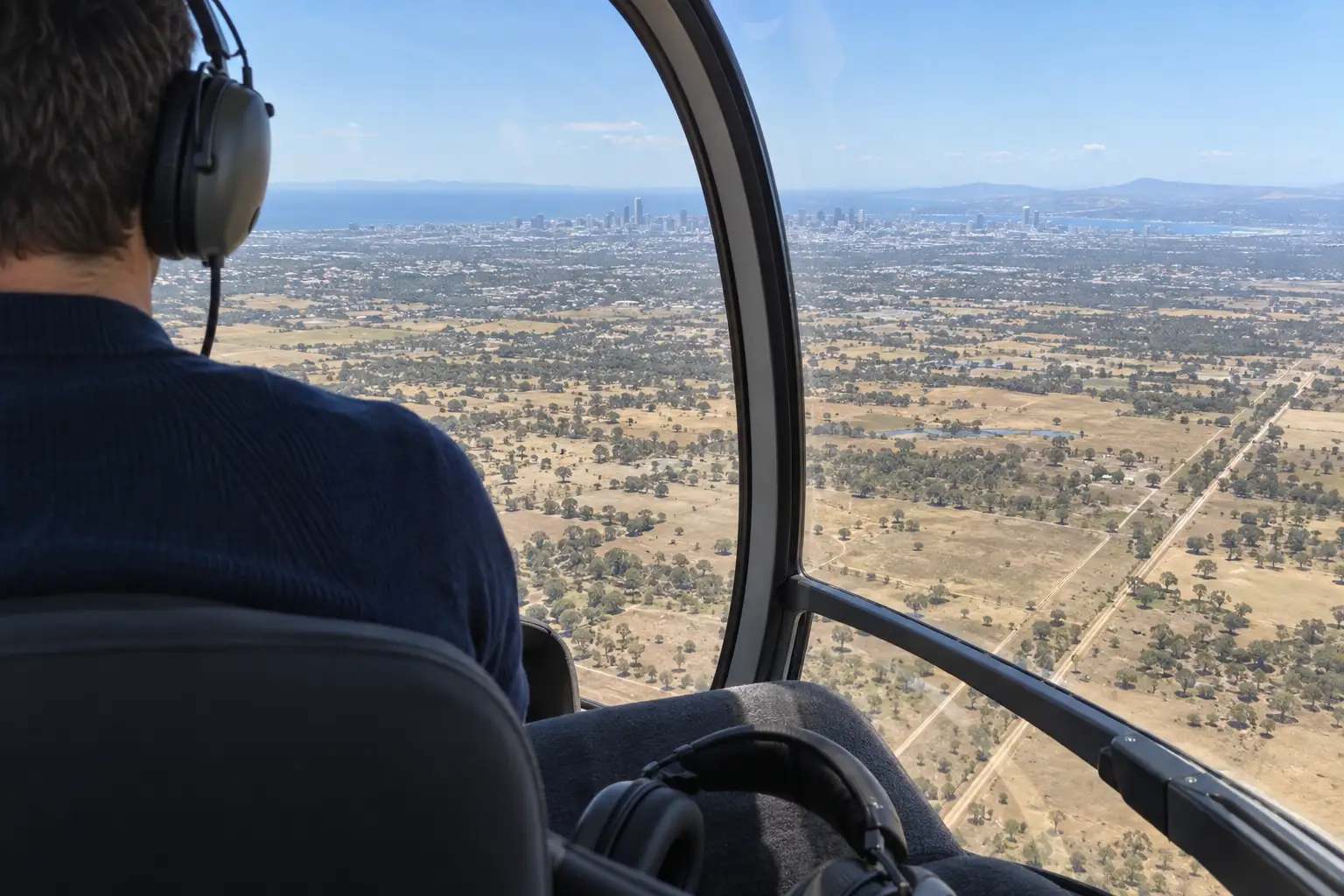 From the back seat, past a passenger's shoulder and headset, the plains and a distant city through the curved canopy