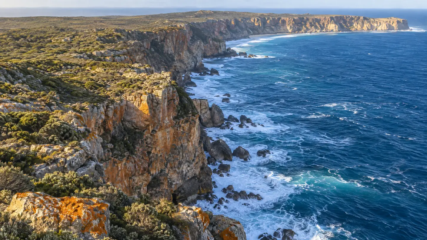 Tall orange and grey sea cliffs on the island's south coast, swell breaking white at their feet