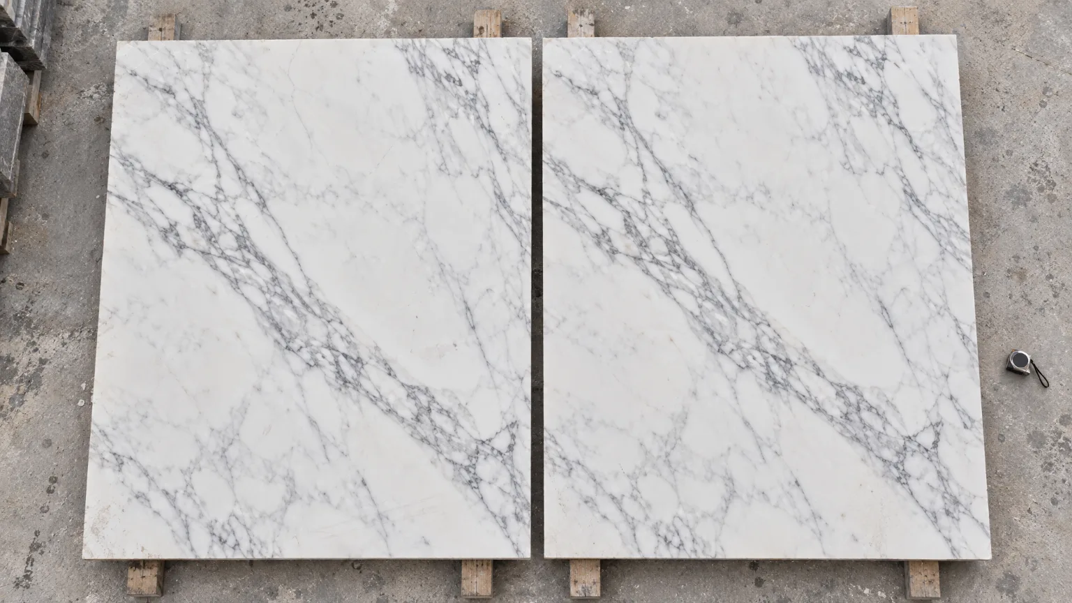 Two white marble slabs with nearly matching grey veins, lying flat side by side in the yard.